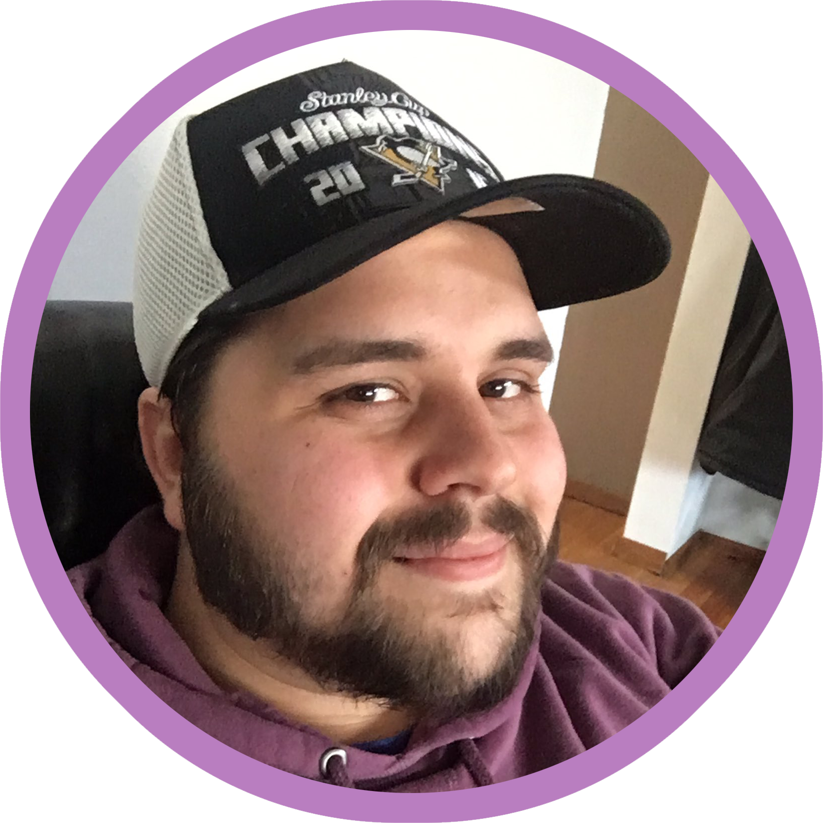 evan scott huber. he has brown eyes and hair, a mustache and beard. he is wearing a purple hoodie and a black pittsburgh penguins hat.